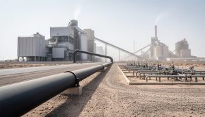Wide low-angle view of a carbon capture retrofit at an industrial cement plant, with connected pipelines and injection infrastructure under an overcast sky